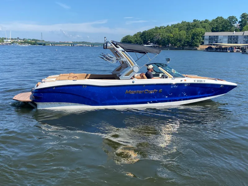 Slide: The Image of 2022 MasterCraft X26 boat cruising on a lake with scenic background. - 1