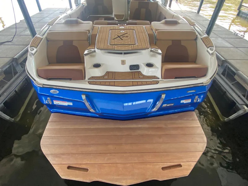 Slide: The Image of 2022 MasterCraft X26 boat with blue exterior and spacious seating, docked in a marina. - 13