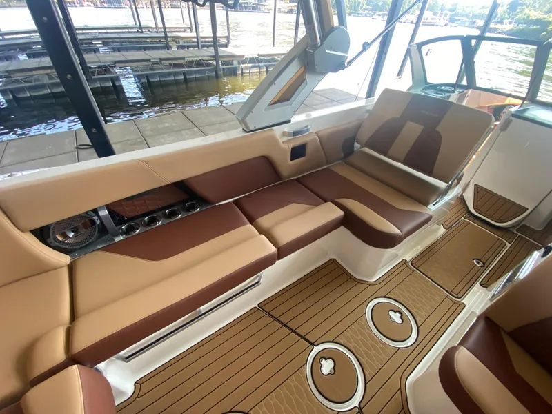 Slide: The Image of 2022 MasterCraft X26 boat interior with brown and tan seating, wood-style flooring, and lake view. - 20