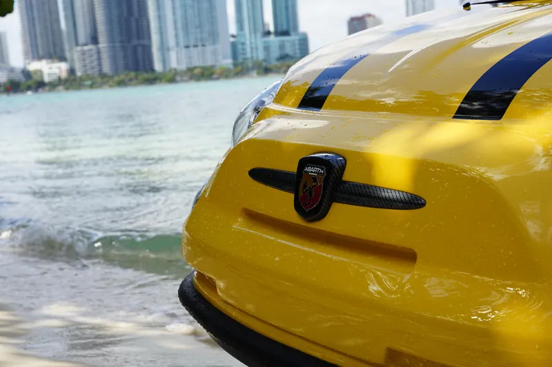 Slide: The Image of Yellow 2025 Fiat 500 Abarth by waterfront, city skyline in background. - 13