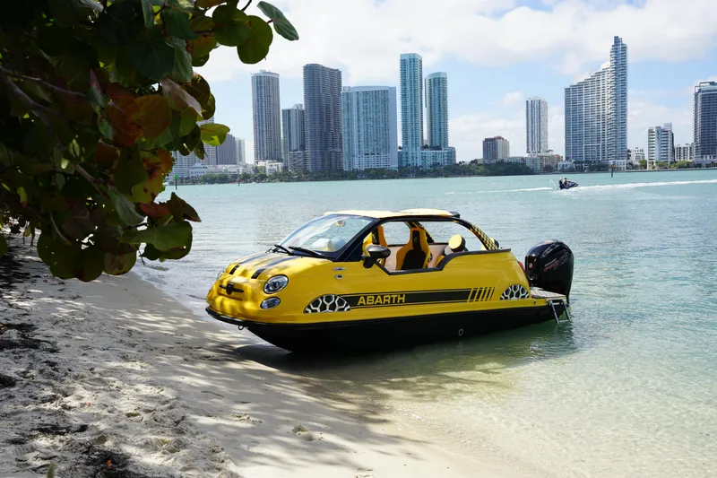 Slide: The Image of 2025 Car Off-shore Fiat 500 Abarth on beach with city skyline in background. - 4