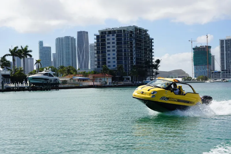 Slide: The Image of Yellow Car Off-shore Fiat 500 Abarth 2025 on water, city skyline in background. - 6
