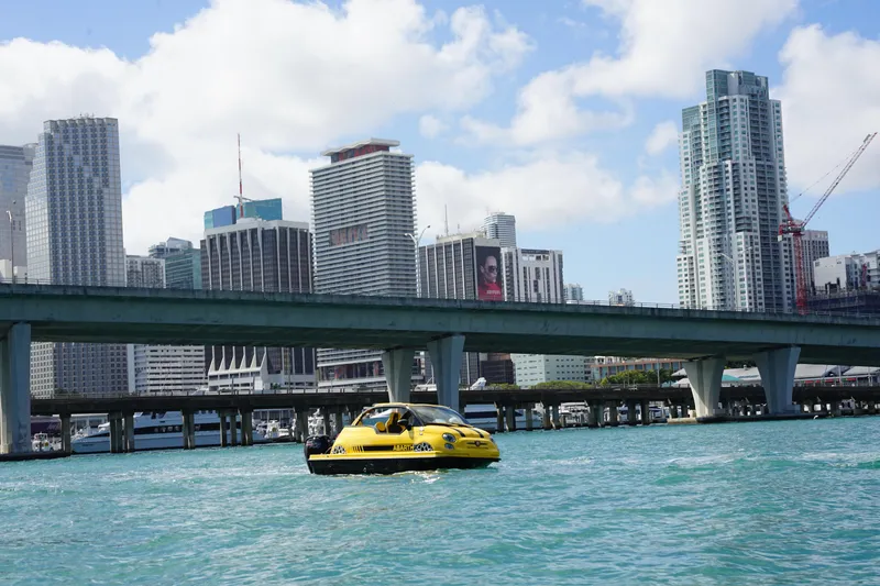 Slide: The Image of Yellow Car Off-shore Fiat 500 Abarth on water, city skyline in background, 2025 model. - 10