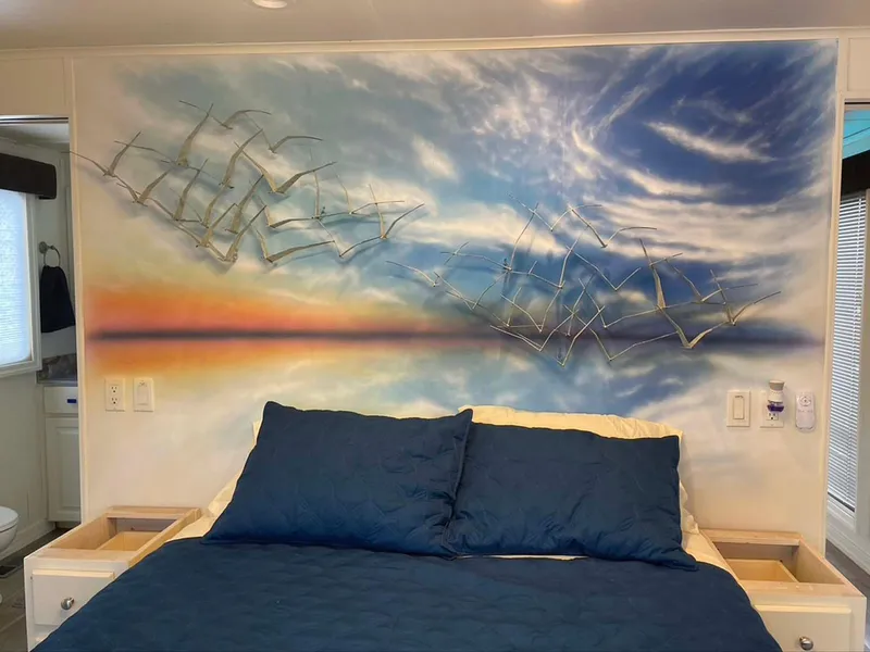 Slide: The Image of Bedroom with blue bedding, sunset mural, and metal bird wall art in a Thoroughbred 6516 model. - 14