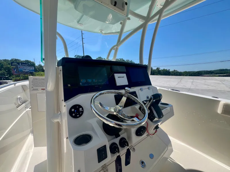 Slide: The Image of 2023 Sailfish 290 CC boat dashboard with steering wheel and controls under clear blue sky. - 12
