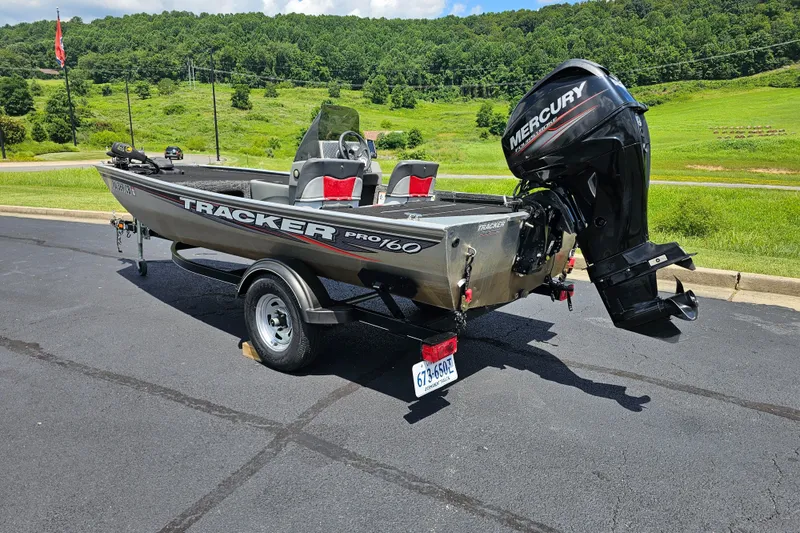 Slide: The Image of 2016 Tracker PRO160 boat with Mercury engine on trailer, parked on asphalt near green landscape. - 4