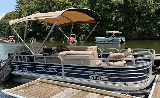 Slide: The Image of 2023 Sun Tracker Fishin' Barge 20 DLX pontoon boat docked on a serene lake. - 2