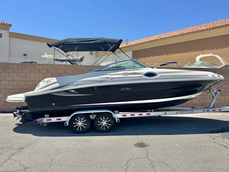 The Image of 2005 Sea Ray 240 Sundeck boat on trailer, parked outdoors, under clear blue sky. - 0