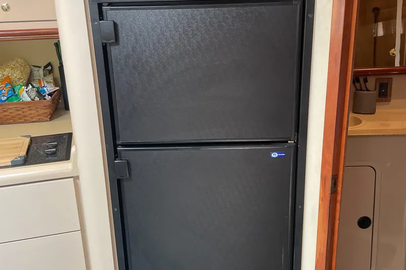 Slide: The Image of Black refrigerator in 2000 Cruisers Yachts 3870 Express kitchen, with snacks on the counter. - 32