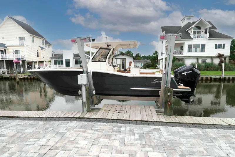 Slide: The Image of 2023 Scout 277 LXF boat docked by waterfront homes under a cloudy sky. - 1