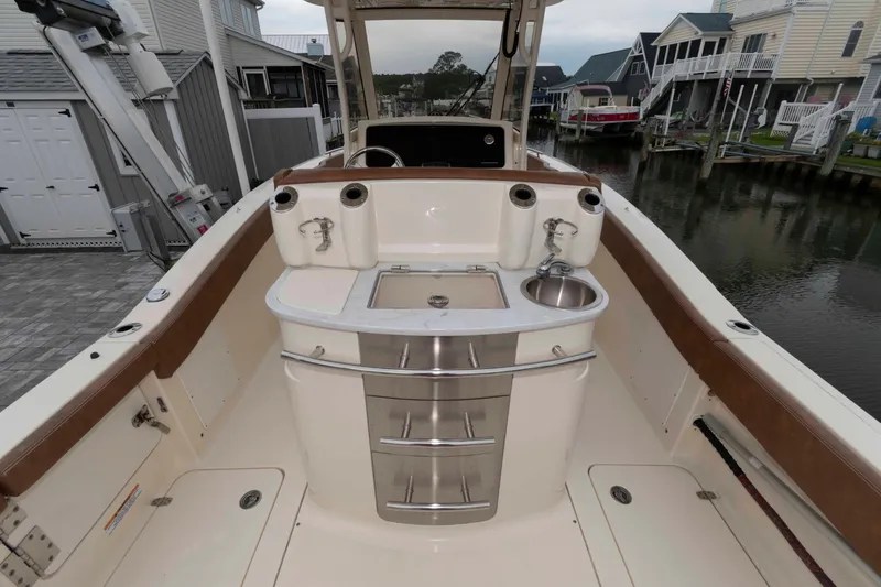 Slide: The Image of 2023 Scout 277 LXF boat interior with sink and storage, docked by waterfront homes. - 18