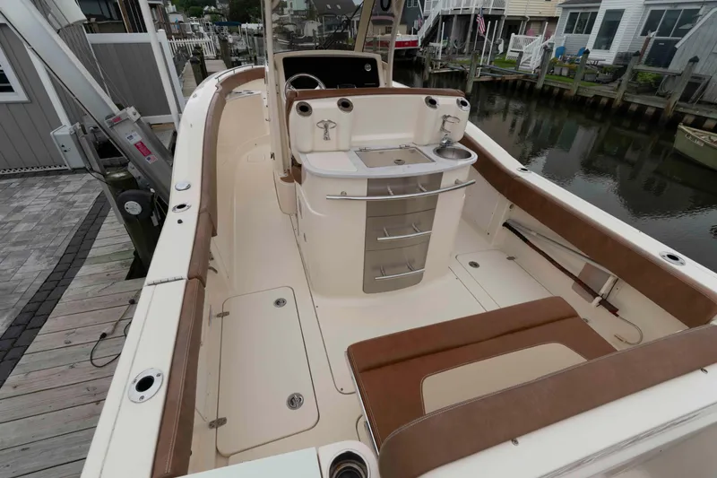 Slide: The Image of 2023 Scout 277 LXF boat interior with seating and storage, docked by waterfront homes. - 7