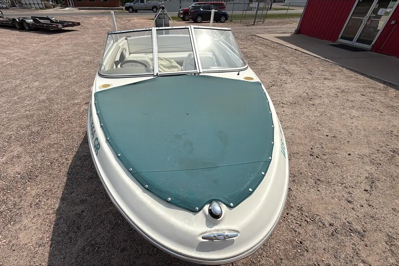 Slide: The Image of 1999 Bayliner 1800 Capri boat with green cover, parked on gravel. - 4