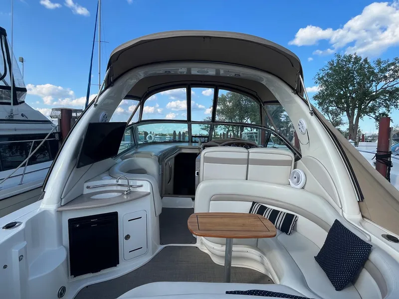 Slide: The Image of 2002 Sea Ray 320 Sundancer interior with seating, table, and kitchenette under a clear blue sky. - 10