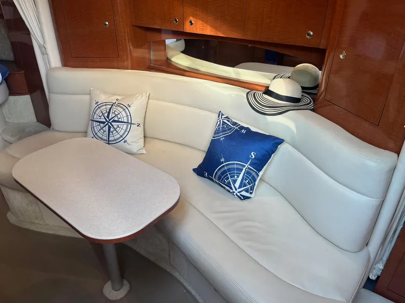 Slide: The Image of Interior of 2002 Sea Ray 320 Sundancer with white seating, nautical pillows, and a table. - 29