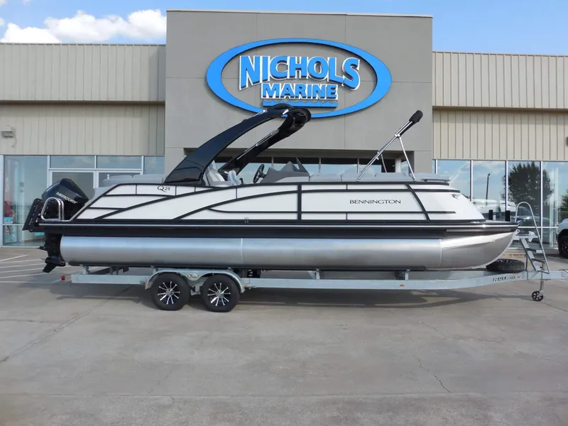 The Image of A sleek Bennington 25 QFBA pontoon boat on a trailer in front of a building with "Nichols Marine" signage. - 1
