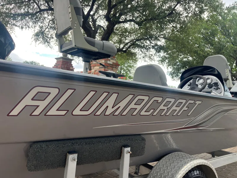 Slide: The Image of 2012 Alumacraft Pro 165 boat with seating, steering wheel, and logo, parked outdoors. - 13