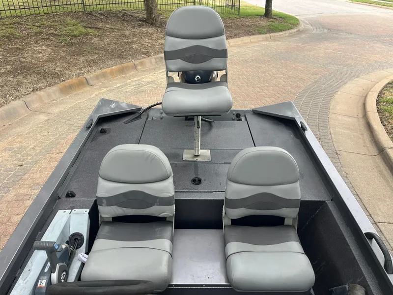 Slide: The Image of 2012 Alumacraft Pro 165 boat interior with three gray seats on a paved area. - 22