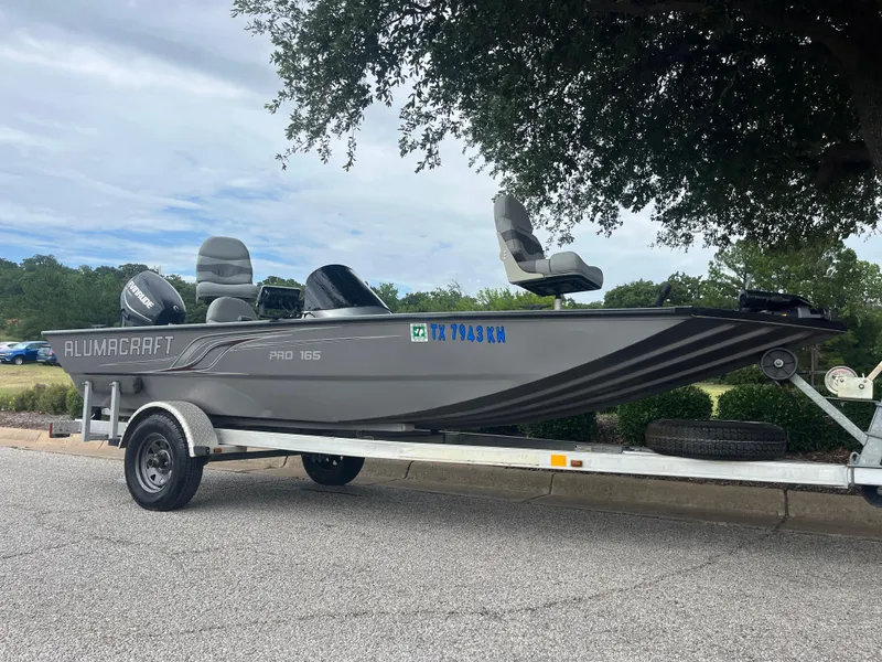 Slide: The Image of 2012 Alumacraft Pro 165 boat on trailer, parked outdoors under a tree. - 27