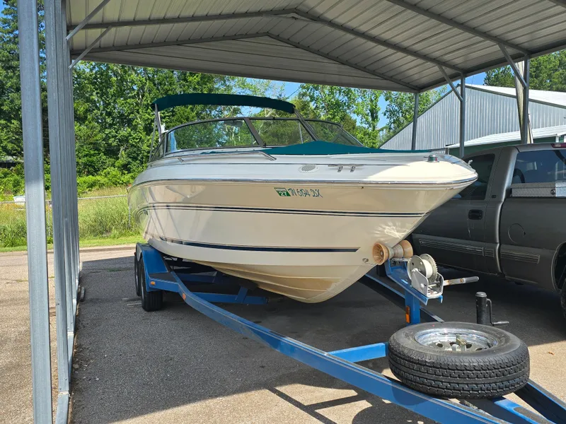 Slide: The Image of 1998 Sea Ray 210br boat on trailer under metal canopy, parked beside a vehicle. - 3