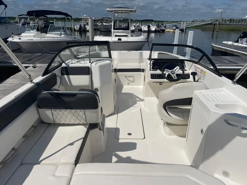 Slide: The Image of 2023 Bayliner DX 2200 boat interior at marina, featuring seating and steering console. - 4