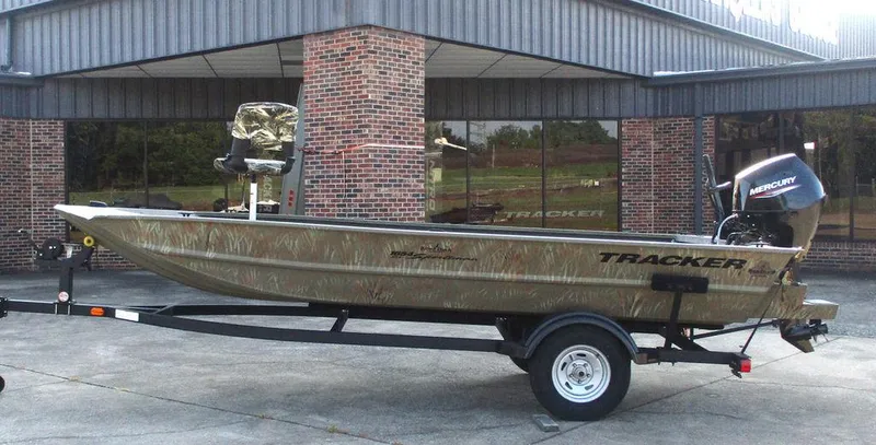 The Image of 2025 Tracker GRIZZLY® 1654 T Sportsman boat on trailer, parked outside a building. - 1