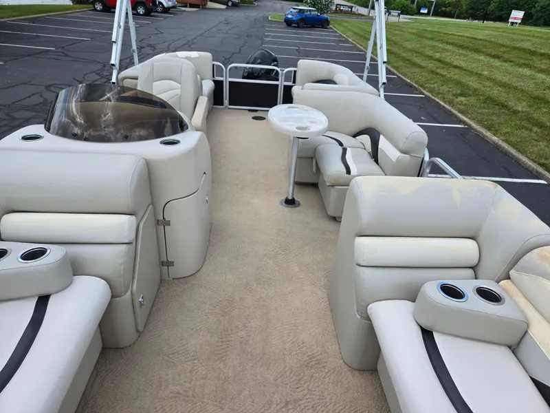 Slide: The Image of 2012 Sweetwater 2486 pontoon boat interior with beige seating and cup holders in a parking lot. - 11