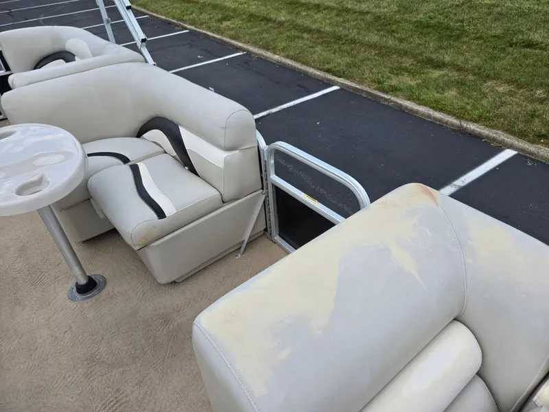 Slide: The Image of Sweetwater 2486 pontoon boat interior with beige seating and table, parked on asphalt, 2012 model. - 12