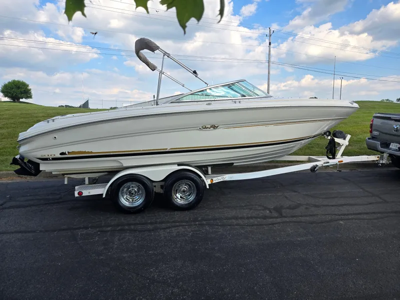 Slide: The Image of 1999 Sea Ray 210 BR boat on trailer, parked outdoors under a partly cloudy sky. - 4