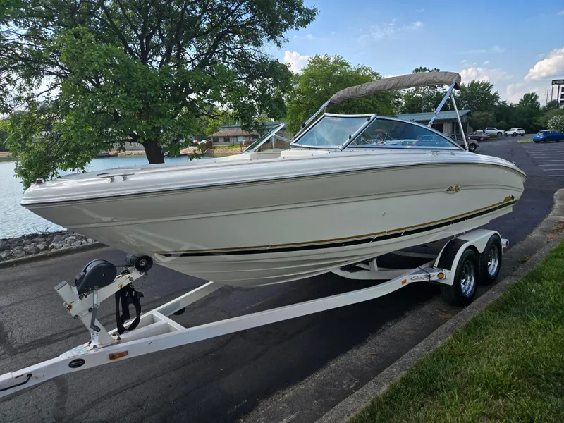Slide: The Image of 1999 Sea Ray 210 BR boat on trailer near a lake, surrounded by trees. - 8