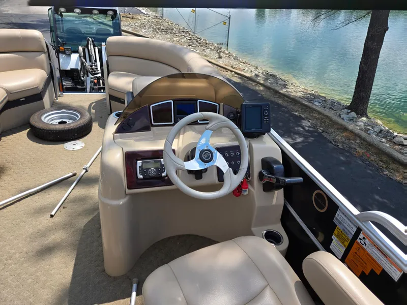 Slide: The Image of 2014 South Bay 522 E pontoon boat interior with steering wheel and seating by a lake. - 22