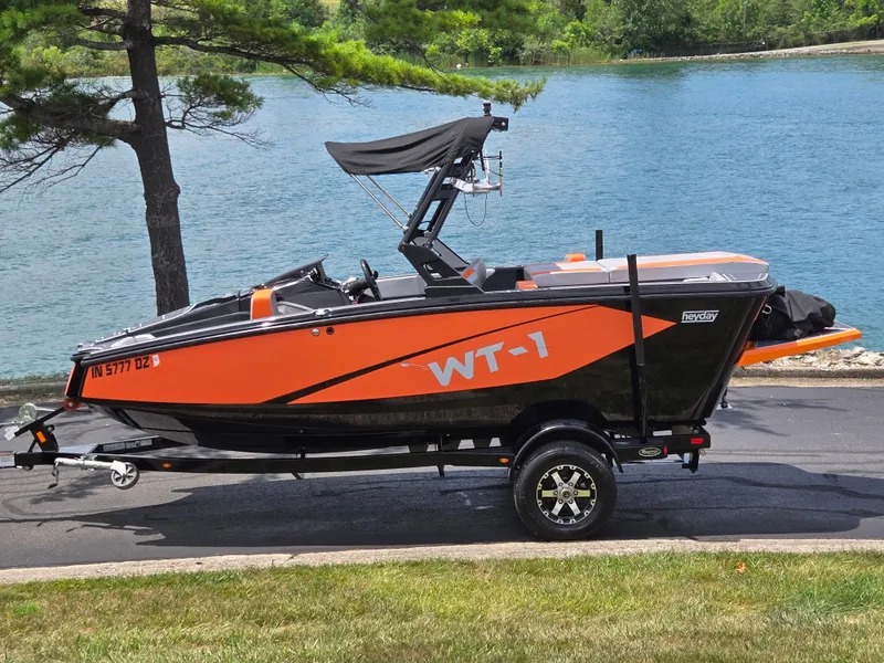 The Image of 2016 Heyday WT-1 boat on trailer by a lake, featuring orange and black design. - 0