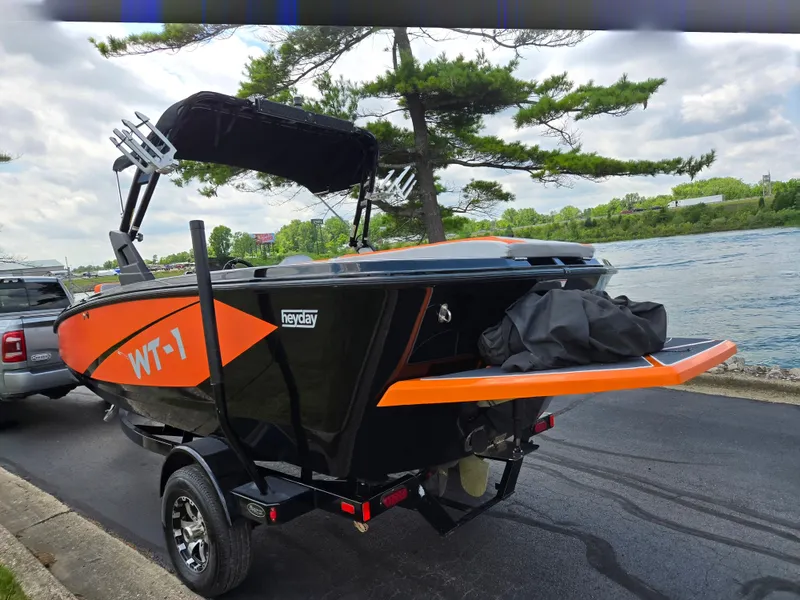 Slide: The Image of 2016 Heyday WT-1 boat on trailer by riverside, featuring vibrant orange and black design. - 1
