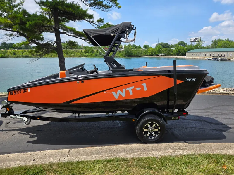 Slide: The Image of 2016 Heyday WT-1 boat on trailer by a lake, featuring orange and black design. - 8