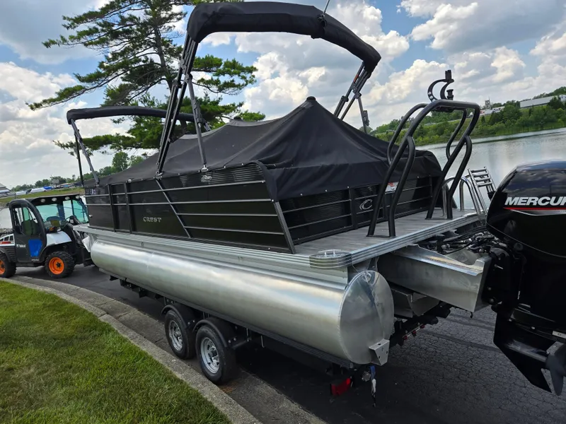 Slide: The Image of 2022 Crest Classic DLX 220 pontoon boat on trailer by a lake, under a cloudy sky. - 4