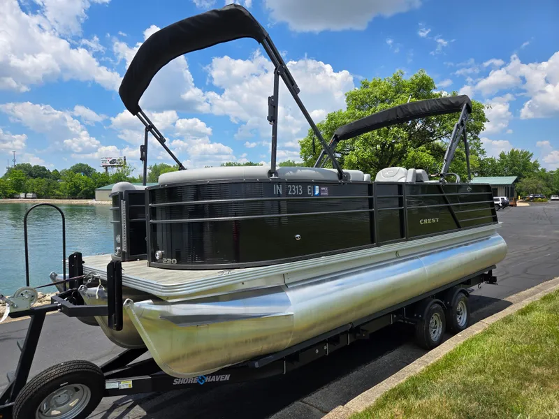 Slide: The Image of 2022 Crest Classic DLX 220 pontoon boat on trailer by a lake under blue sky. - 9