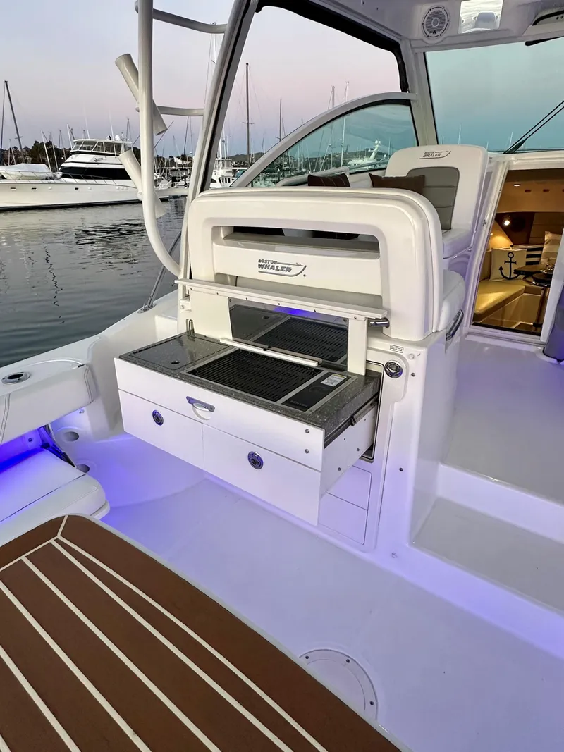 Slide: The Image of 2014 Boston Whaler 315 Conquest boat interior with grill and seating area at marina. - 13