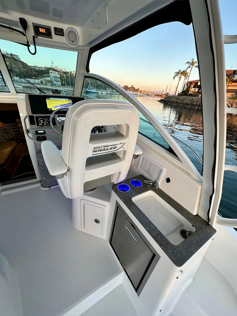Slide: The Image of 2014 Boston Whaler 315 Conquest helm with steering wheel, sink, and waterfront view. - 23