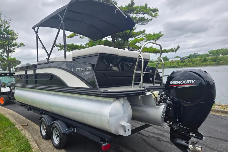 Slide: The Image of 2022 Lowe SS 230 CL pontoon boat with Mercury engine on trailer by a lake. - 2