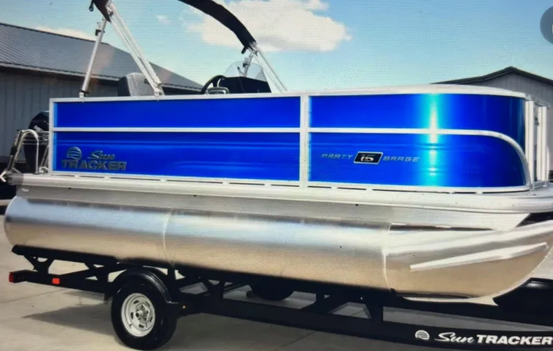 The Image of 2026 Sun Tracker Party Barge 16 DLX pontoon boat on trailer, blue and silver design. - 1