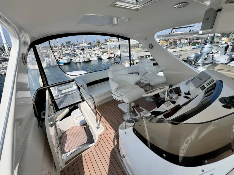 Slide: The Image of 2002 Sea Ray 560 Sedan Bridge yacht interior with helm, white seating, and marina view. - 22