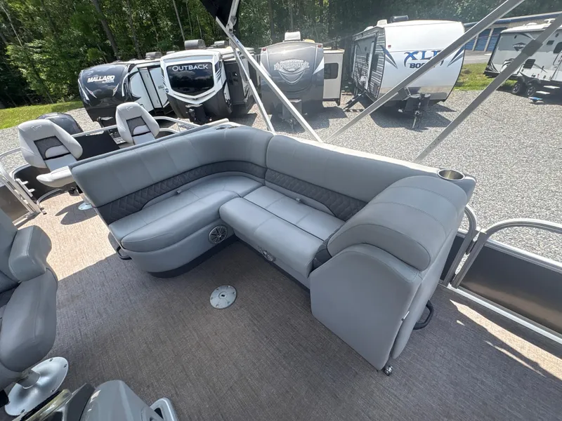 Slide: The Image of 2021 Ranger Reata 220F pontoon boat with gray seating and cup holders, parked near RVs. - 11