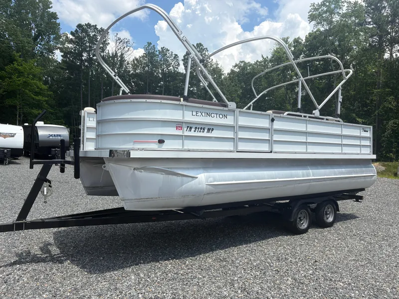 The Image of 2021 Lexington 321 pontoon boat on trailer, parked on gravel lot with trees in background. - 1