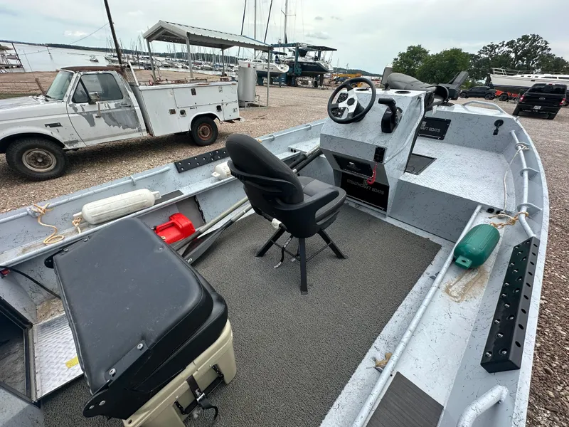 Slide: The Image of 2023 StealthCraft Stealthweld 18 boat interior with steering console and seating, parked near marina. - 8