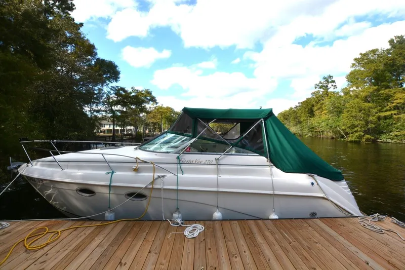 Slide: The Image of 1999 Rinker 270 Fiesta Vee boat docked on a serene lake with green canopy. - 3