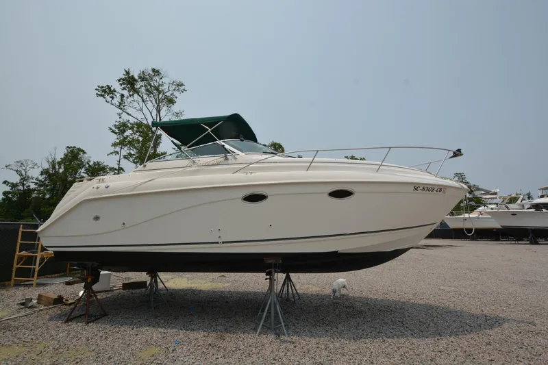 Slide: The Image of 1999 Rinker 270 Fiesta Vee boat on stands, with green canopy, in a gravel lot. - 4