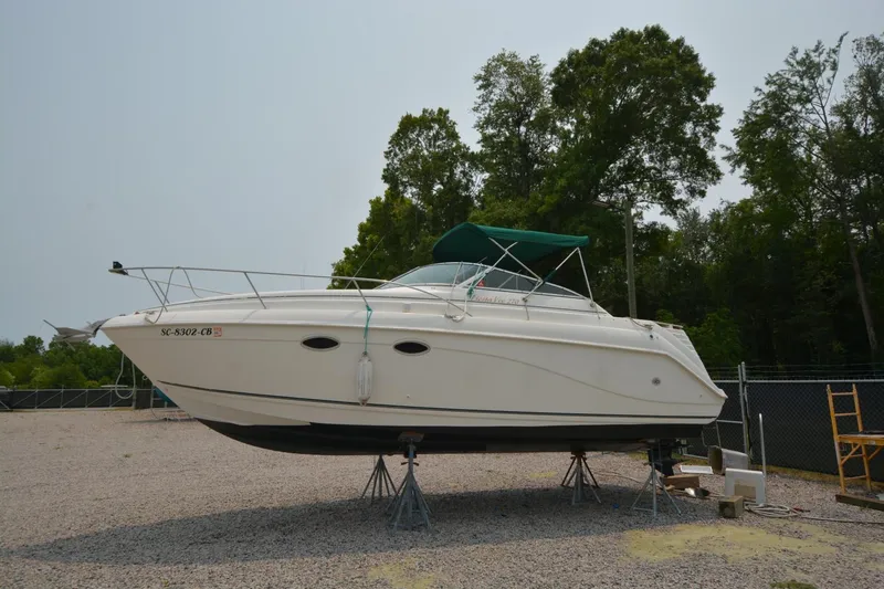 Slide: The Image of 1999 Rinker 270 Fiesta Vee boat on stands, with green canopy, in a gravel lot. - 5