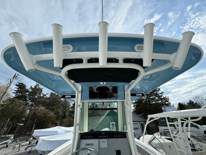 Slide: The Image of Boston Whaler 280 Outrage 2025 boat with rod holders and blue canopy under a cloudy sky. - 19