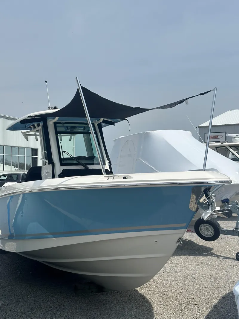 Slide: The Image of 2025 Boston Whaler 280 Outrage boat with blue hull and black canopy, parked outdoors. - 34