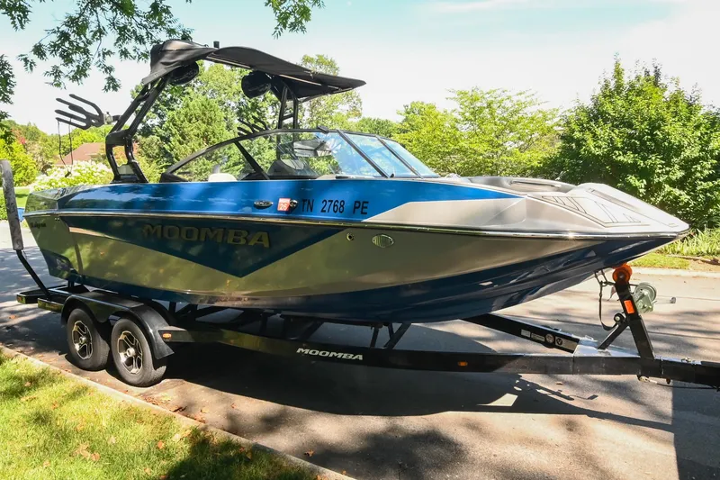 Slide: The Image of 2021 Moomba Kaiyen boat on trailer, parked on a sunny street with lush greenery. - 2